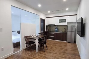 A compact kitchen with a dining area, a refrigerator, and a flat-screen TV. - Phong Lan Building and Apartments (Haiphong)