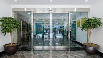 A modern entrance with glass doors, potted plants, and a marble floor.