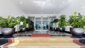 Eine moderne Lobby mit Marmorboden, rotem Teppich und je einer großen Pflanzengruppe an beiden Seiten des Eingangs.