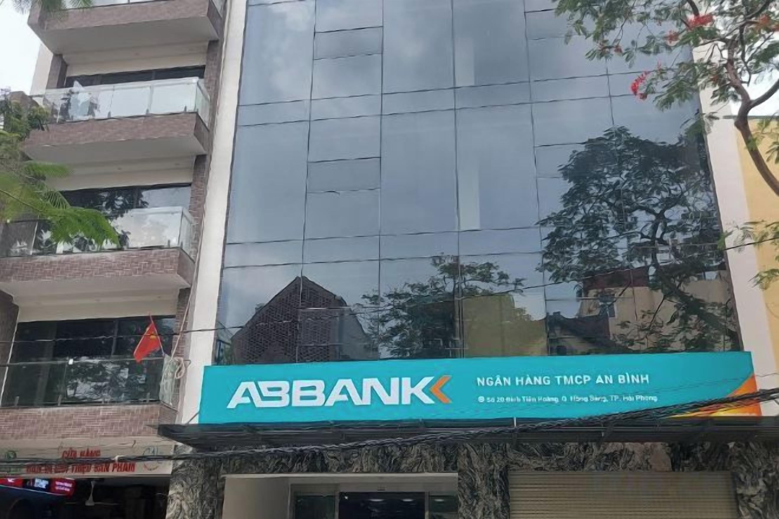 A building with a sign for 'ABBANK' and a reflection of trees on its glass facade.