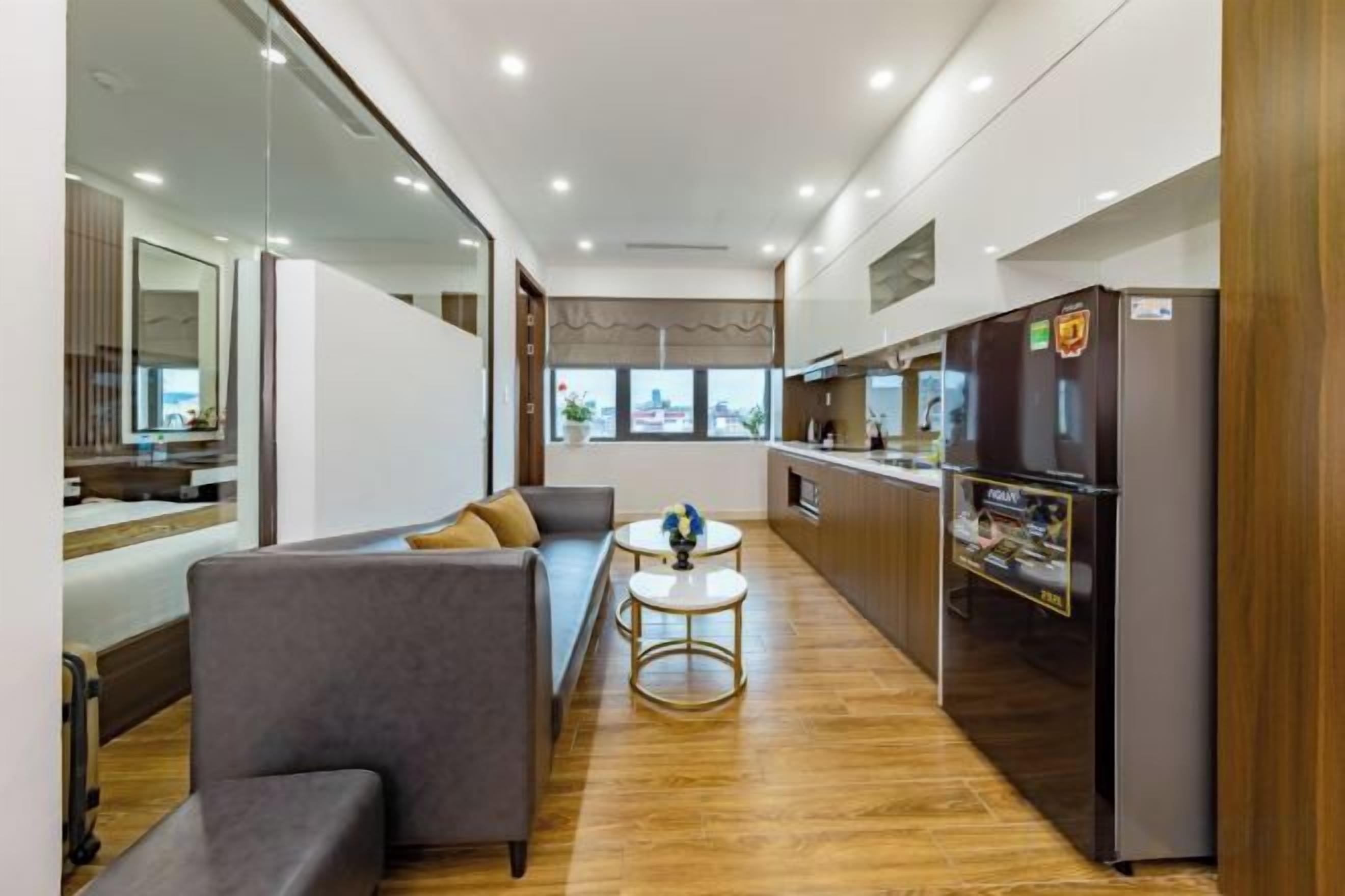 A modern living room with a sofa, a coffee table, and a kitchen area with a refrigerator.