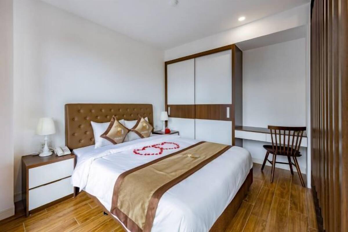 Camera d'albergo con un letto grande, una scrivania, una sedia e un comodino con lampada e telefono.