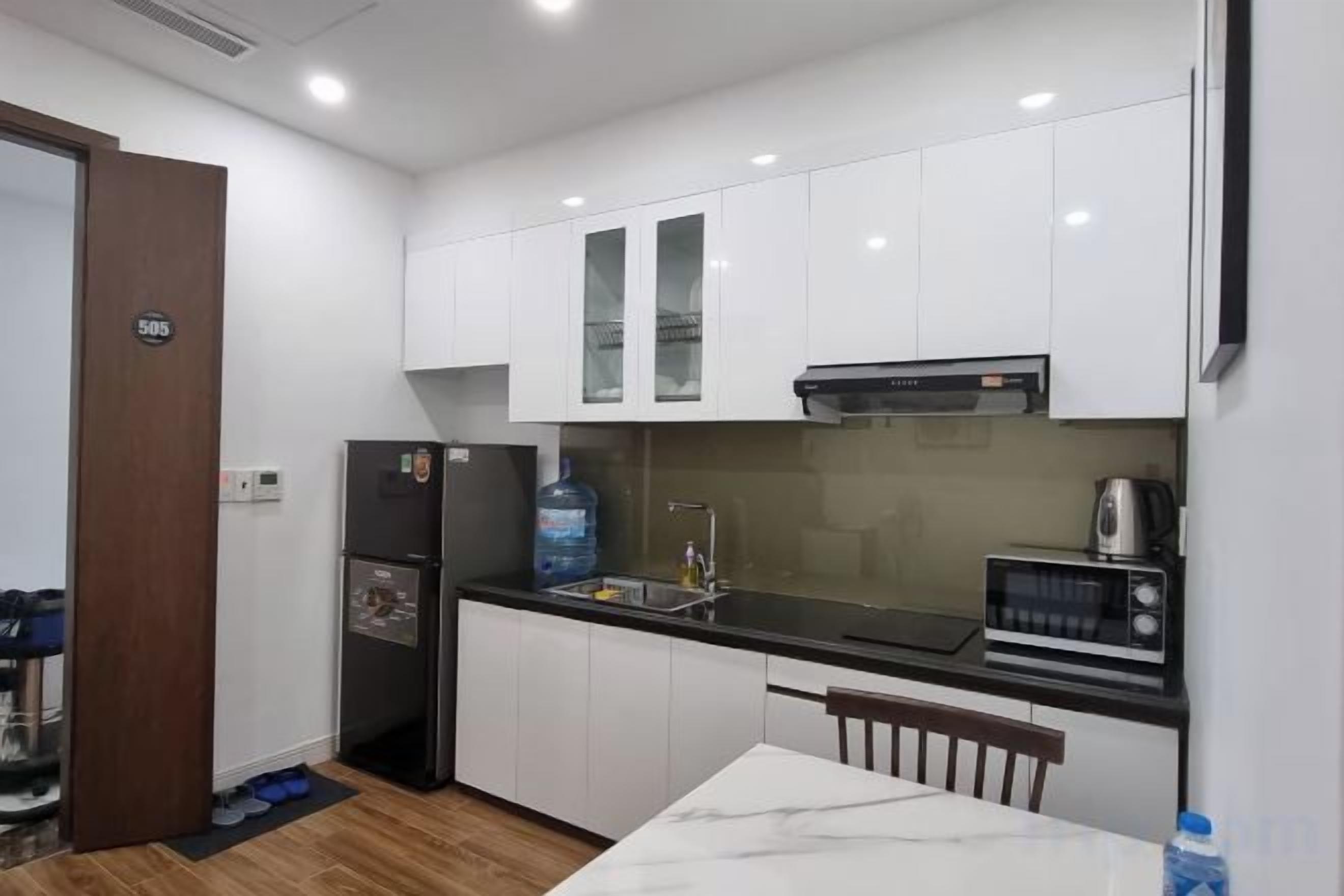 A compact kitchen with white cabinets, a black countertop, a refrigerator, a microwave, and a sink.