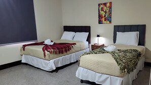 Two double beds with white bedding and dark headboards, a small bedside table with a lamp, and a colorful abstract painting on the wall. - Be happy hotel Gt (Guatemala City)