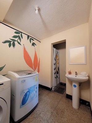 A hotel bathroom with a washing machine, a sink, and a shower curtain. - Be happy hotel Gt (Guatemala City)