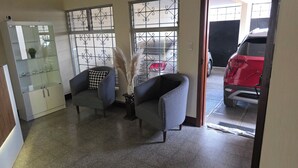 A room with two armchairs, a glass cabinet, and a window with metal bars. - Be happy hotel Gt (Guatemala City)