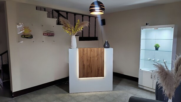 A reception desk with a wooden panel, a vase with yellow flowers, and a modern pendant light. - Be happy hotel Gt (Guatemala City)