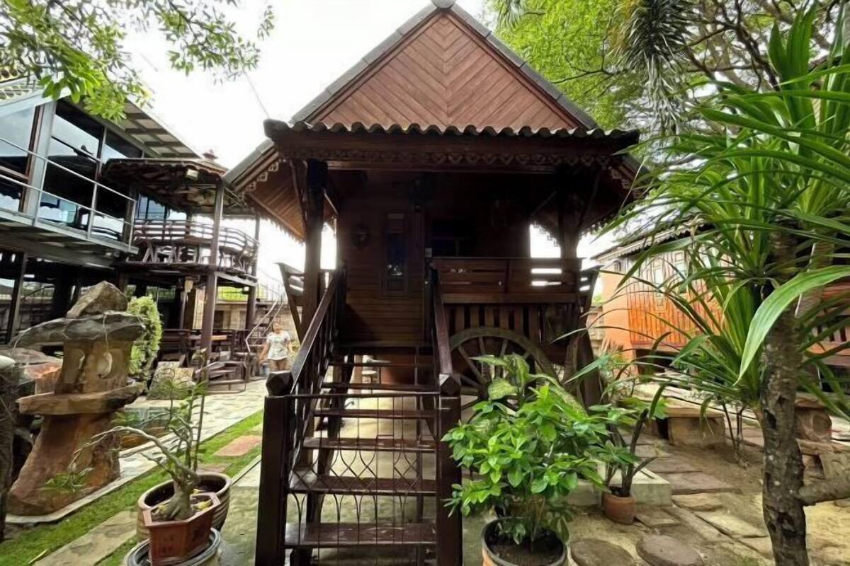 A wooden structure with a staircase leading to a covered area, surrounded by potted plants and a stone pathway.