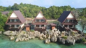 A row of three bungalow-style buildings on stilts over clear water, surrounded by lush greenery. - Sienna Resort (Maratua)
