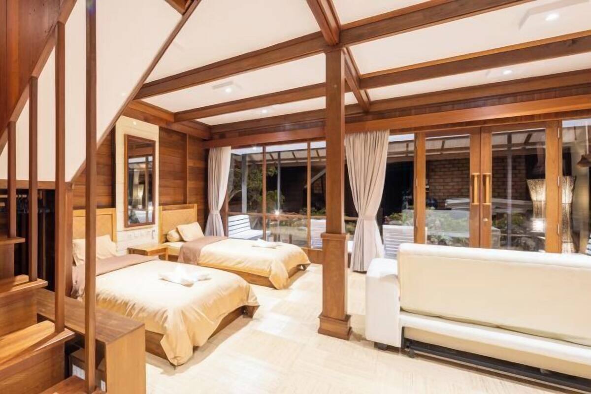 A spacious bedroom with two beds, a sofa, wooden beams, and large windows.