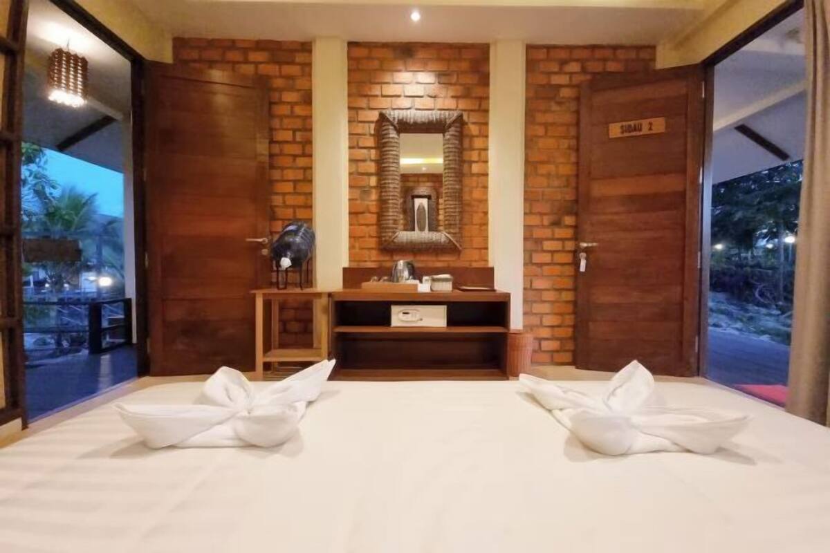 A hotel room with a brick wall, a wooden vanity, a mirror, and a bed with towels.