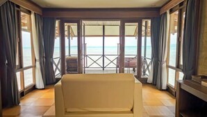 A room with a sofa, large windows, and a view of the beach. - Sienna Resort (Maratua)