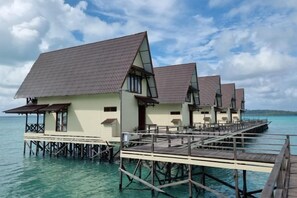 Bungalows op palen met een houten terras en een helder uitzicht op de turquoise zee.