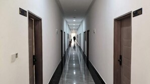 Un long couloir étroit, avec des portes de chaque côté, et une personne qui le traverse.
