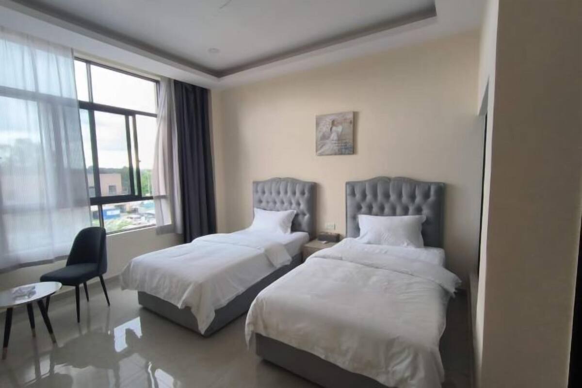 A hotel room with two beds, a chair, a table, and a window with curtains.