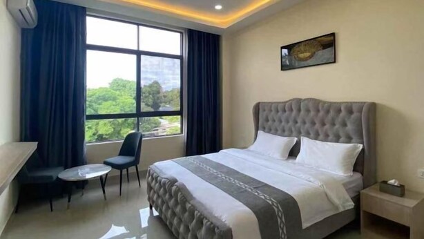 Une chambre d’hôtel avec un grand lit, une petite table, deux chaises, une table de chevet et une fenêtre avec des rideaux.