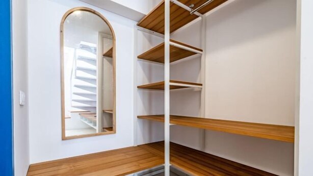 Un coin de pièce avec un banc en bois, un mur blanc et une porte de placard à miroir.