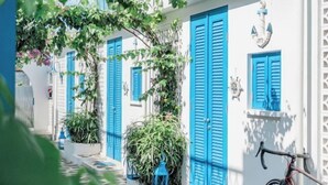 Une rue étroite bordée de bâtiments blancs aux volets bleus, avec un vélo et des plantes en pot.