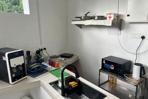 A kitchenette with a coffee machine, a dishwashing station, and a shelf with a first aid kit. - Hillview Ipoh (Ipoh)