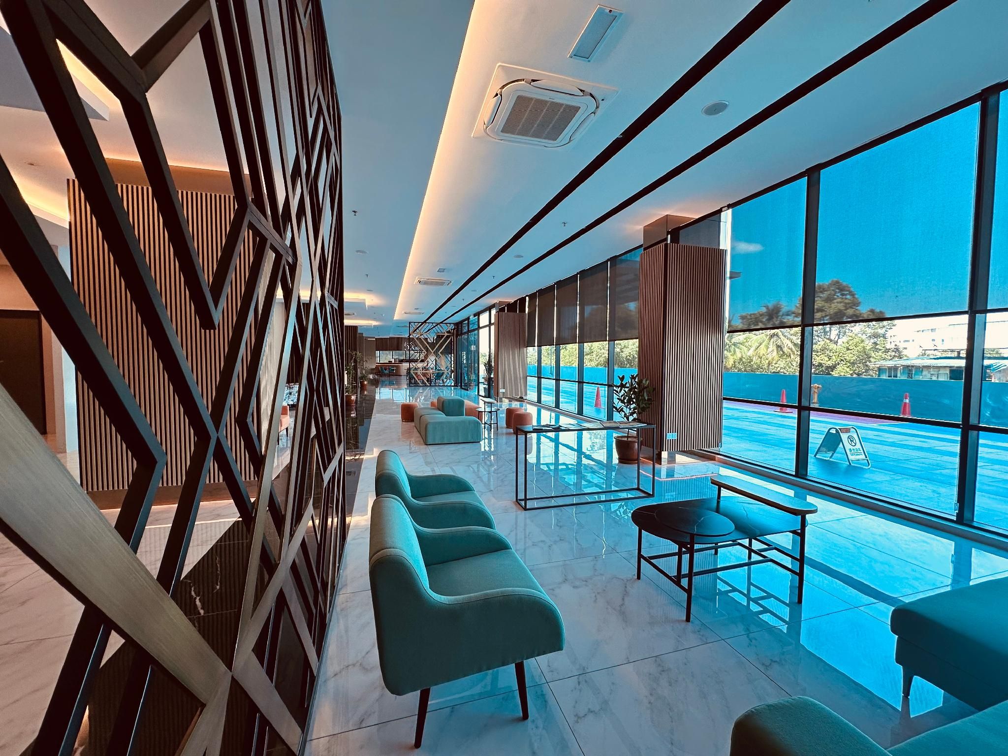 A modern hotel lobby with a long reception desk, seating area with sofas, and large windows offering a view of the outdoors.