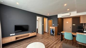 A modern apartment with a flat-screen TV, a dining area with two chairs, a kitchen with a black refrigerator, and a built-in washer and dryer.