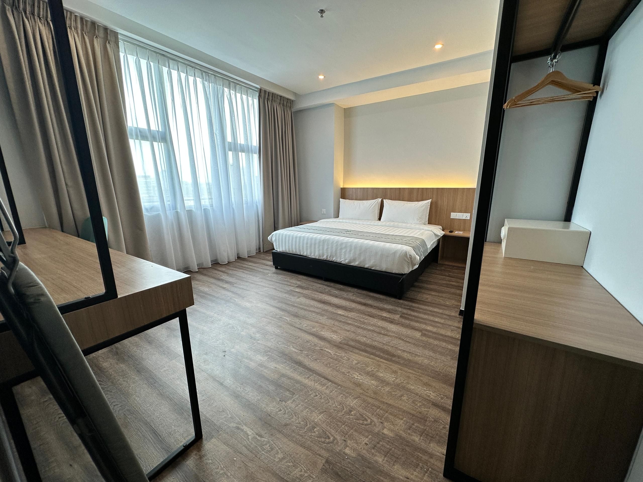 A hotel room with a bed, bedside table, and a desk with a chair.