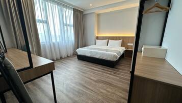 A hotel room with a bed, bedside table, and a desk with a chair.