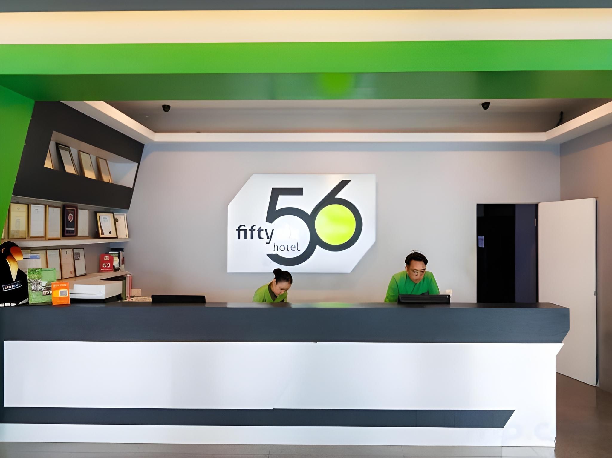 A reception desk with a large sign displaying '56 fifty hotel' and two individuals seated behind it.