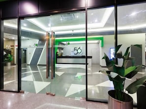 A modern reception area with glass doors, a reception desk, and a green accent wall. - 56 Hotel Block B (Kuching)