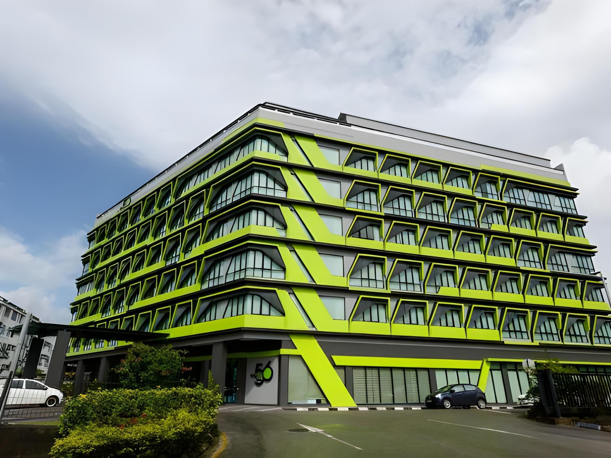 Ein mehrgeschossiges Gebäude mit einer markanten geometrischen Fassade, großen Fenstern und einem Parkplatz davor.