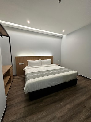 A modern bedroom with a large bed, a wooden headboard, and a built-in desk with drawers. - 56 Hotel Block B (Kuching)