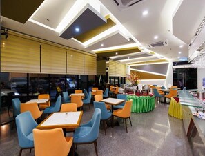 Interno moderno di un ristorante con diversi tavoli e sedie, un'area buffet e un bancone.