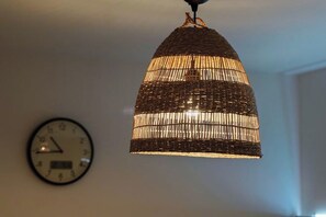 Eine gewebte Pendelleuchte hängt von der Decke, im Hintergrund ist eine Wanduhr zu sehen.