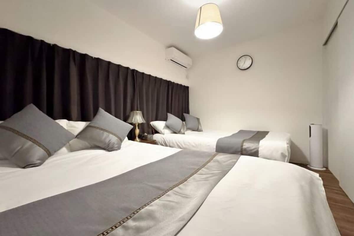 Habitación de hotel con dos camas, una mesita de noche con lámpara, un reloj en la pared y un equipo de aire acondicionado.