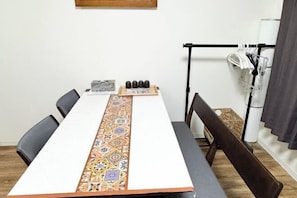 Une table de conférence avec un chemin de table à motifs, des chaises, une petite table sur laquelle sont posés divers objets, et un présentoir noir avec des objets blancs.