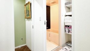 A hallway with a green door, a white door, and a shower area with a white shower curtain. There is a shelf with folded towels and a framed picture on the wall. - Osaka Nimi family house direct KIX airport (Osaka)