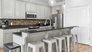 A modern kitchen with white cabinets, a black countertop, stainless steel appliances, and bar stools.