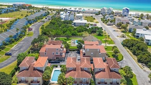 A coastal residential area with multiple two-story houses, a central swimming pool, and a beach in the background.