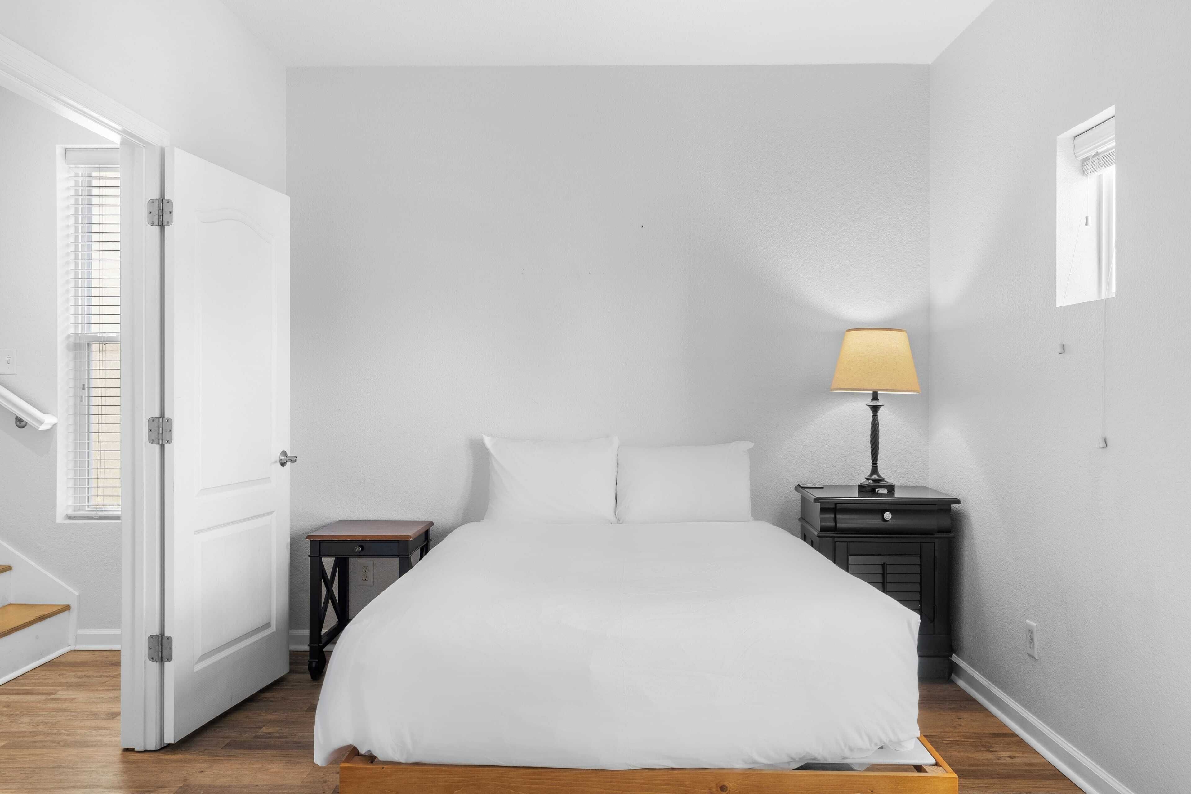 Een slaapkamer met een bed, nachtkastje, lamp en een deur naar een andere kamer.