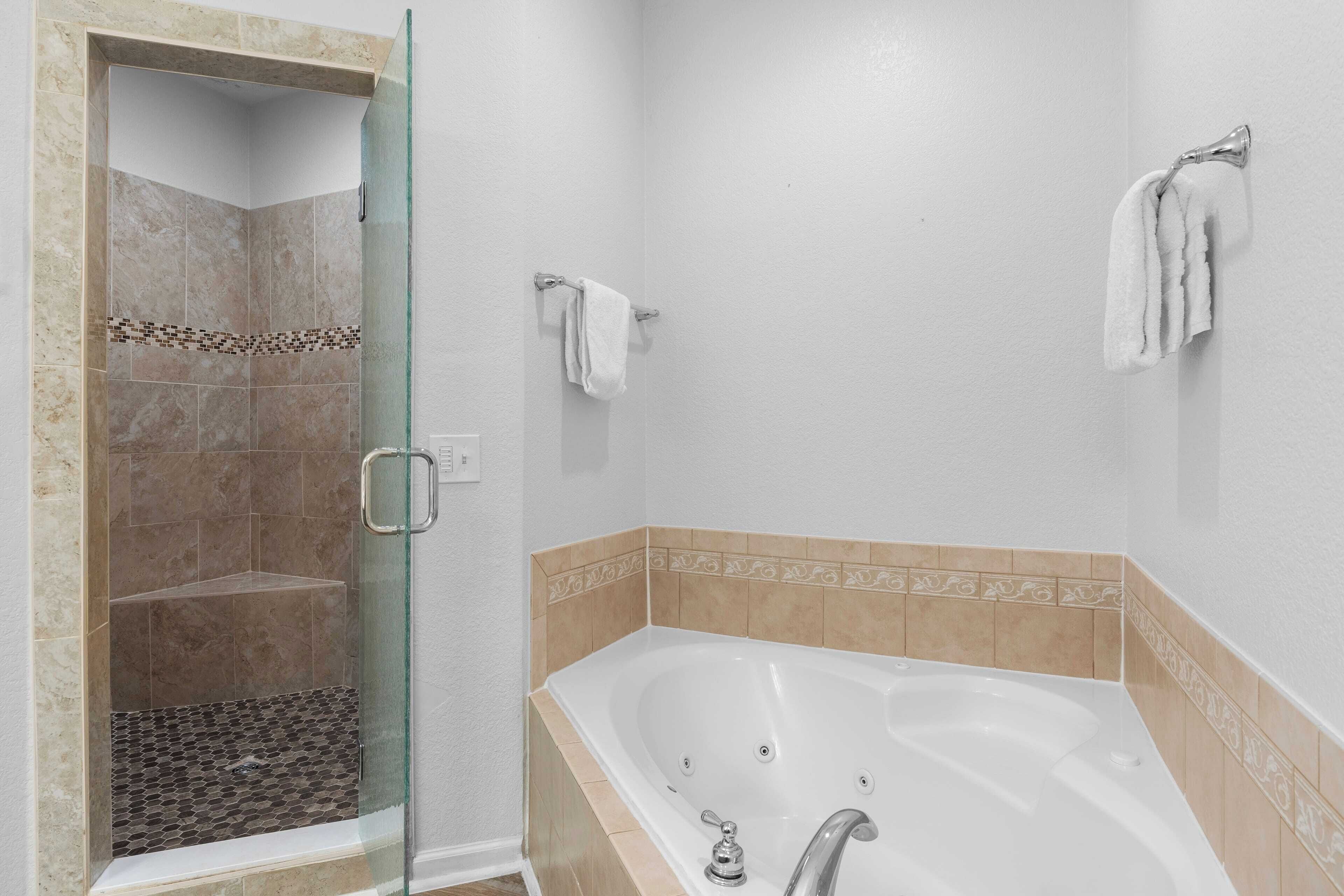 A bathroom with a glass-enclosed shower, a bathtub, and two towel hooks on the wall.