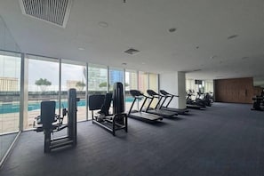 A gym with exercise equipment and large windows overlooking a pool. - The Peak Service Apt By David (Phnom Penh)