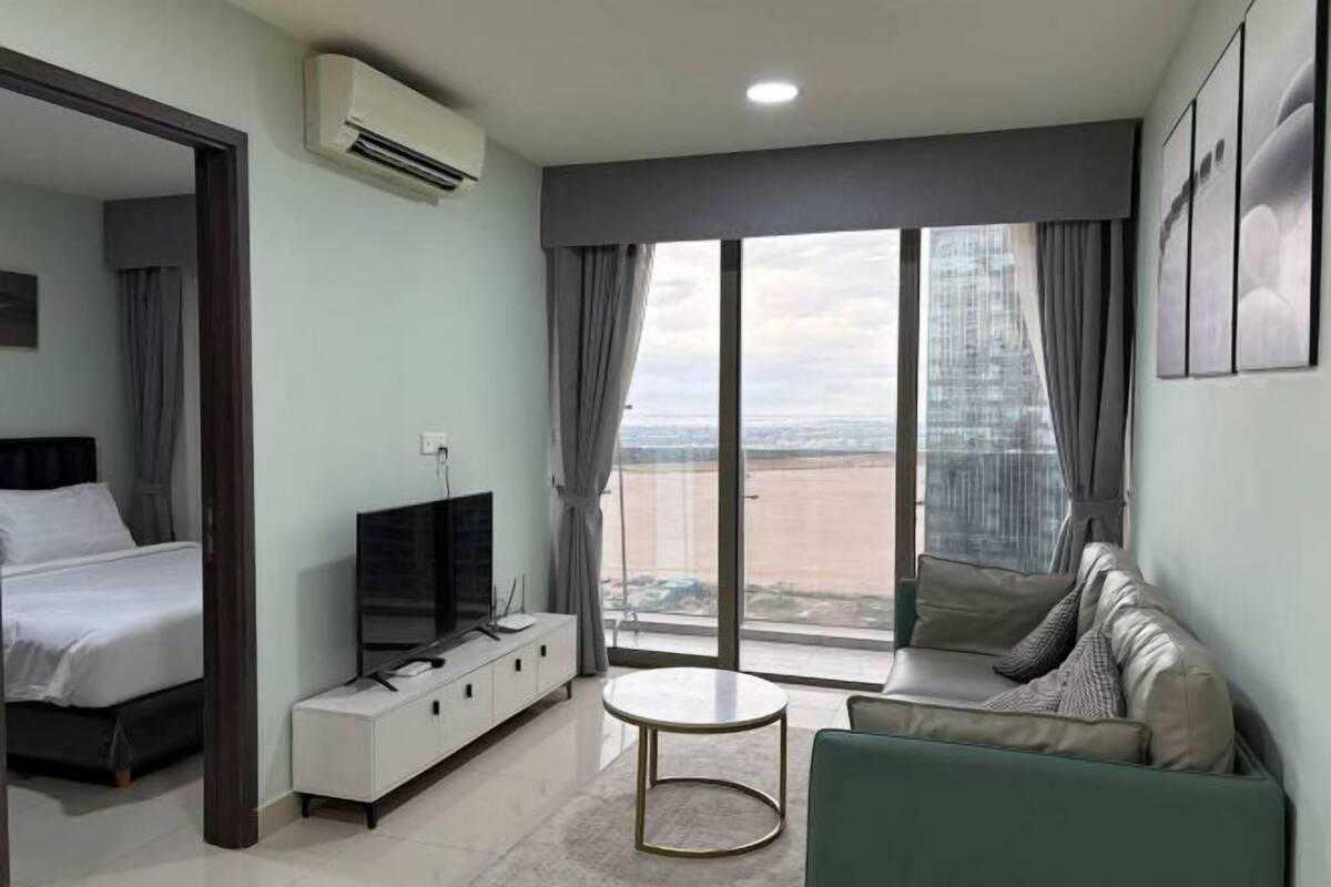 Ein modernes Hotelzimmer mit Bett, Fernseher, Sofa, kleinem Tisch und einem großen Fenster mit Blick auf die Stadt.
