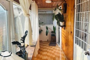 A narrow hallway with wooden flooring, a door with glass panels, and potted plants. - Homieow inn (Dalat)