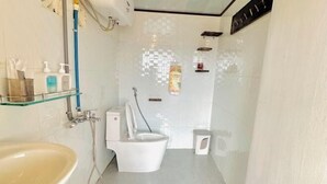 A bathroom with a sink, toilet, shower, and a glass shelf with toiletries. - Homieow inn (Dalat)