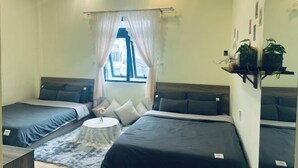 A room with two beds, a small round table, a window with curtains, and a wall-mounted plant shelf. - Homieow inn (Dalat)