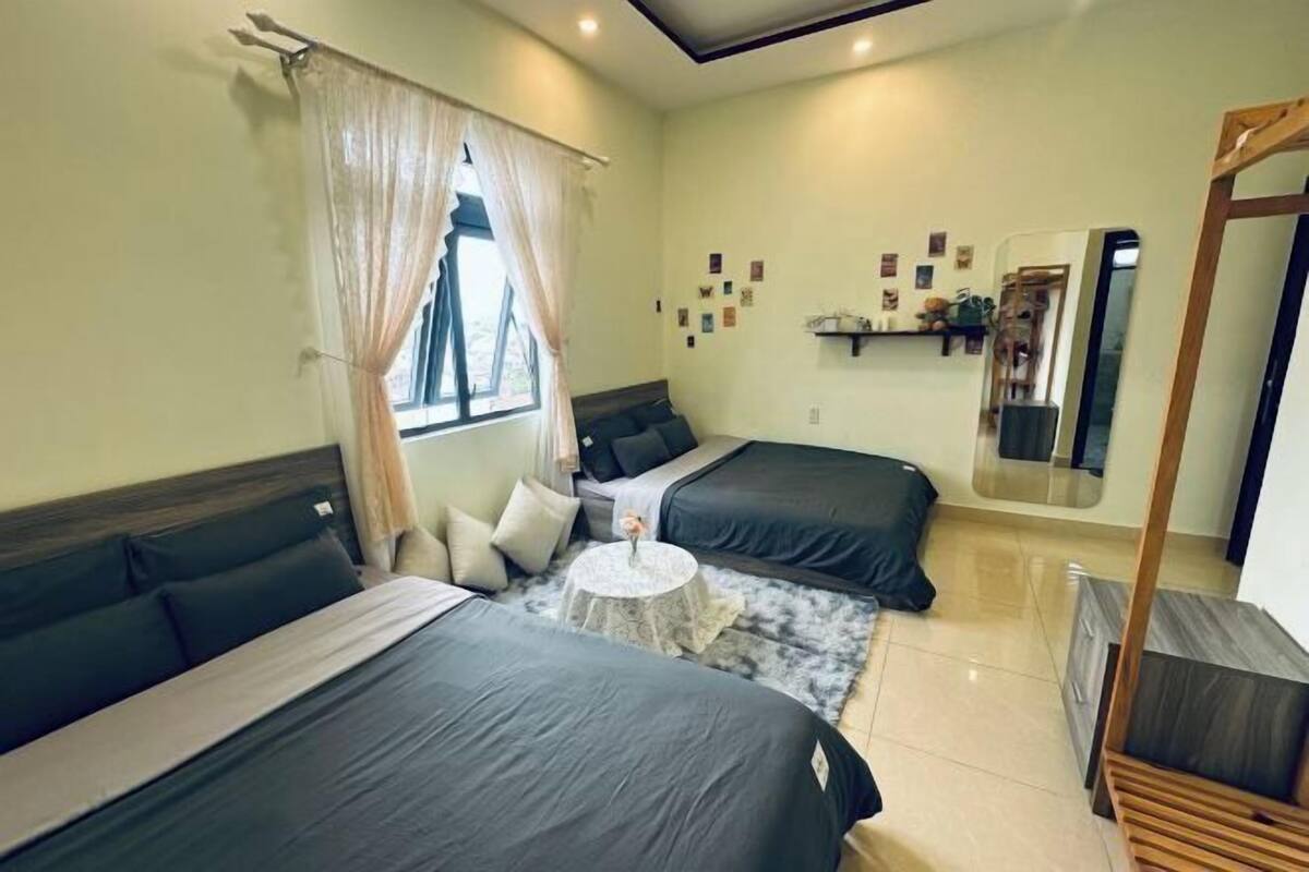 A room with two beds, a round table, a mirror, and a window with curtains.