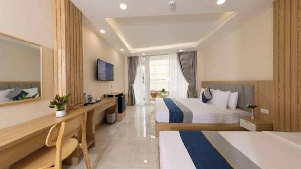 A hotel room with a desk, two beds, a TV, and a large window. - Ben Thanh Luxury Suite Hotel (Ho Chi Minh City)