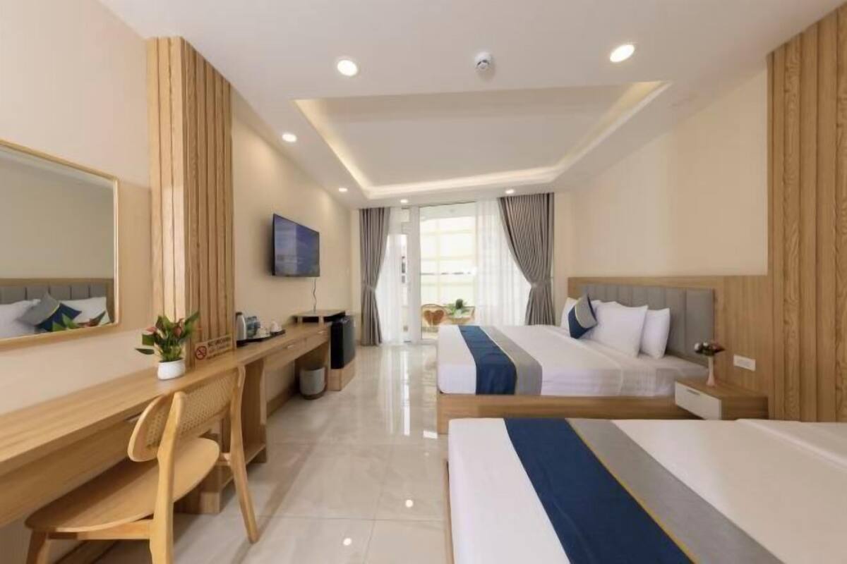 Une chambre d’hôtel équipée d’un bureau, de deux lits, d’une télévision et d’une grande fenêtre.