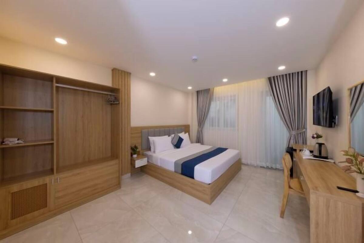 Une chambre d’hôtel moderne avec un grand lit, une armoire en bois, un bureau et une télévision.