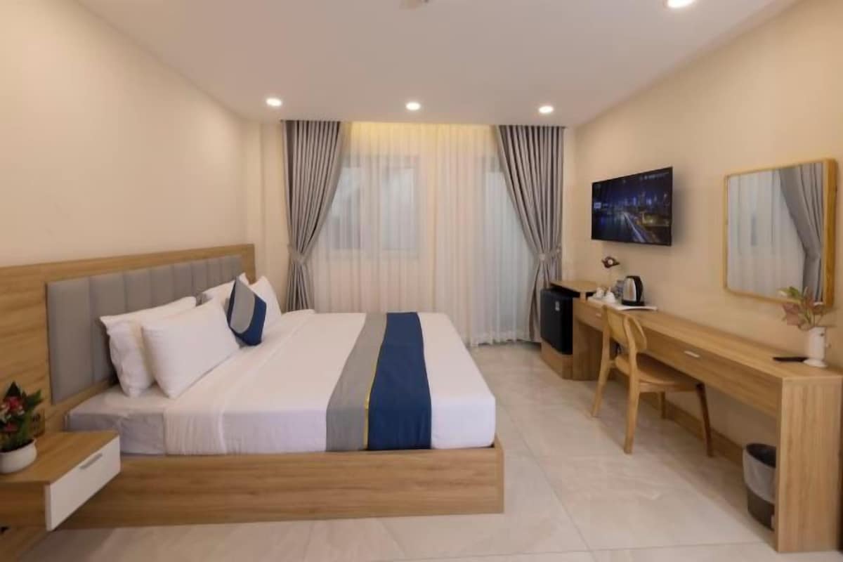 A hotel room with a bed, desk, chair, TV, and curtains.